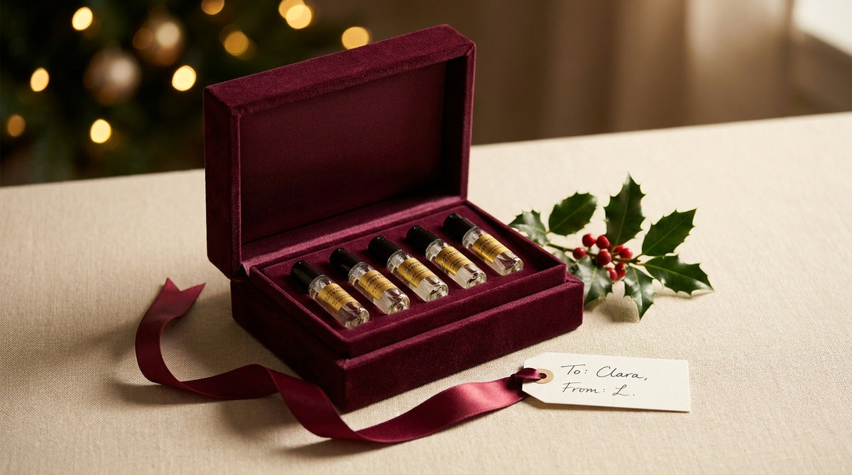 Luxury burgundy velvet gift box with five gold-labeled fragrance vials, satin ribbon, holly sprig