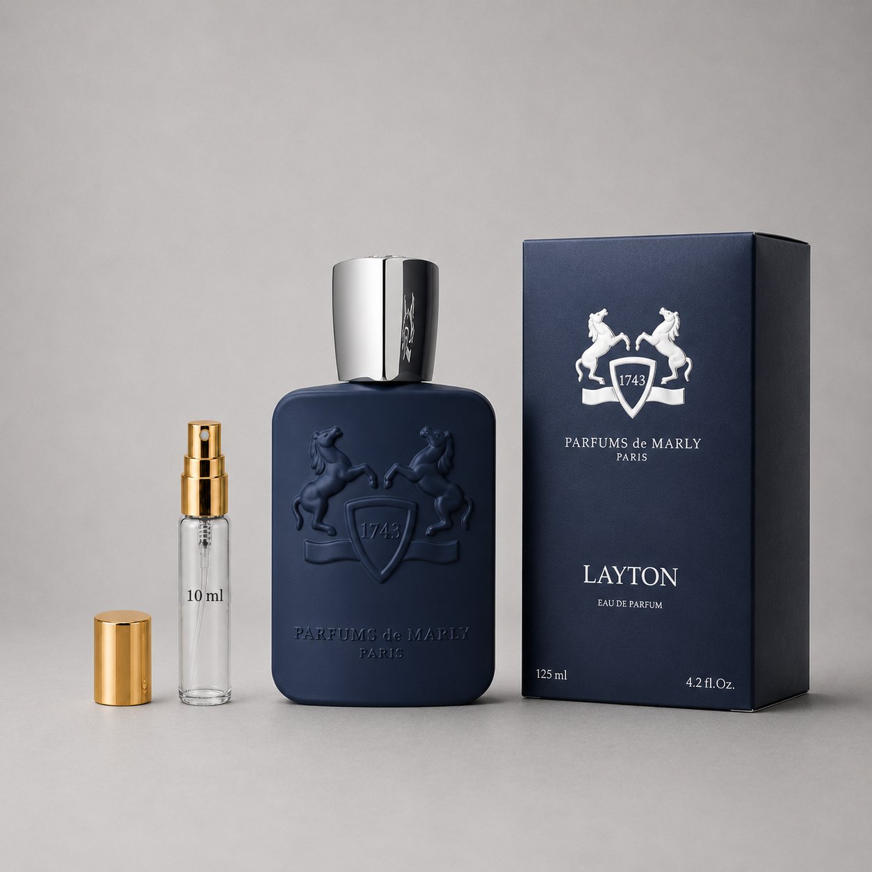 Parfums de Marly Layton sample spray with a 10ml vial, a navy blue bottle, and a matching box, all displayed on a gray backgr