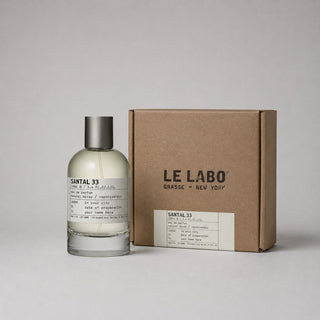 Le Labo Santal 33 Sample Spray in a clear bottle next to a brown cardboard box, featuring minimalist labels and branding.
